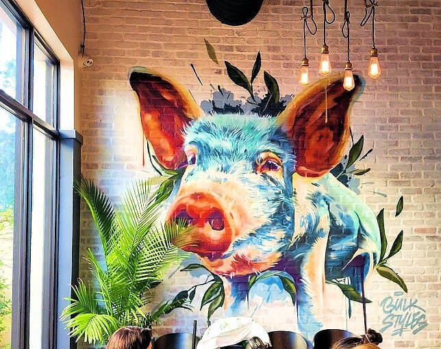 Bulk Styles mural in a commercial space — colorful pig head on brick wall