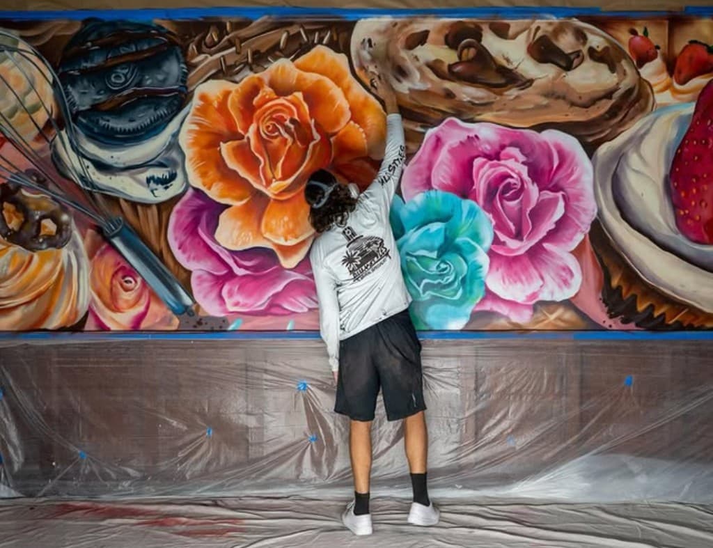 Artist painting a vibrant mural of desserts and roses