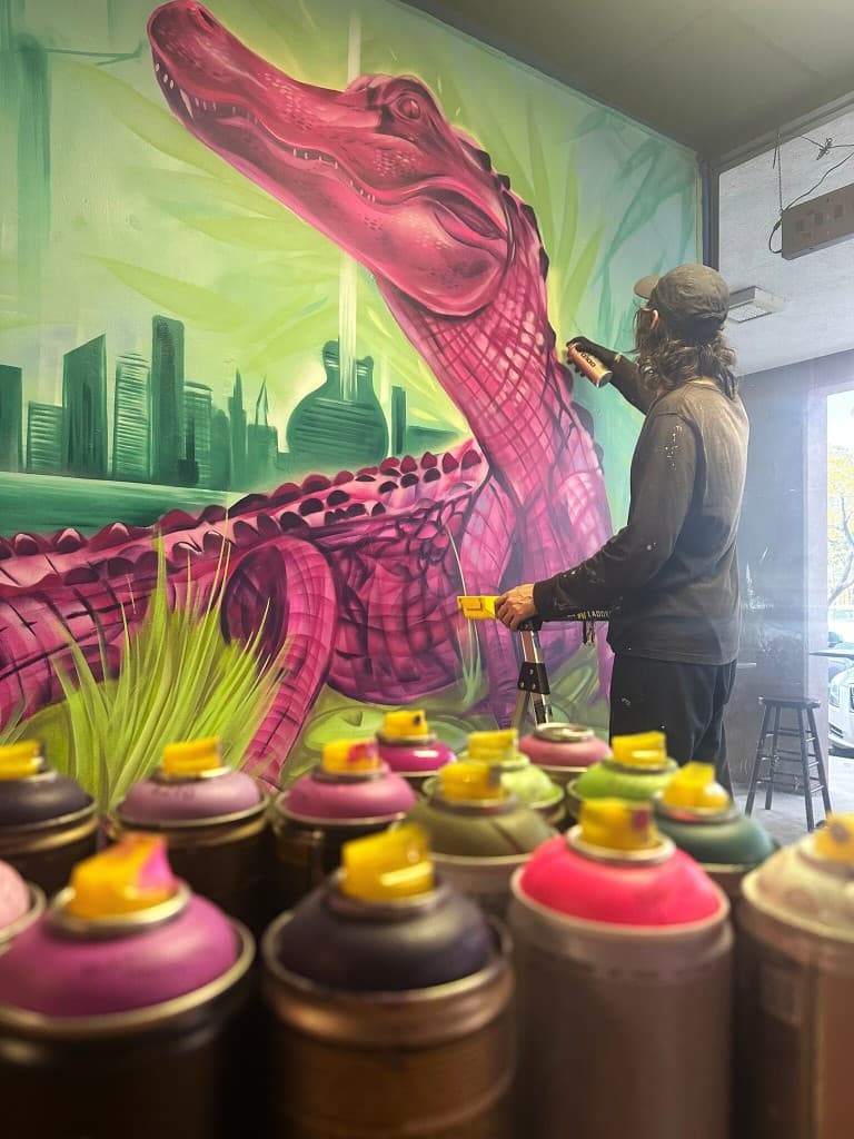 Mural artist Mark Francis of Bulk Styles painting a large colorful mural with spray paint