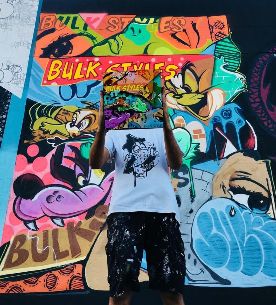 Mural artist Mark Francis of Bulk Styles standing in front of a colorful graffiti mural