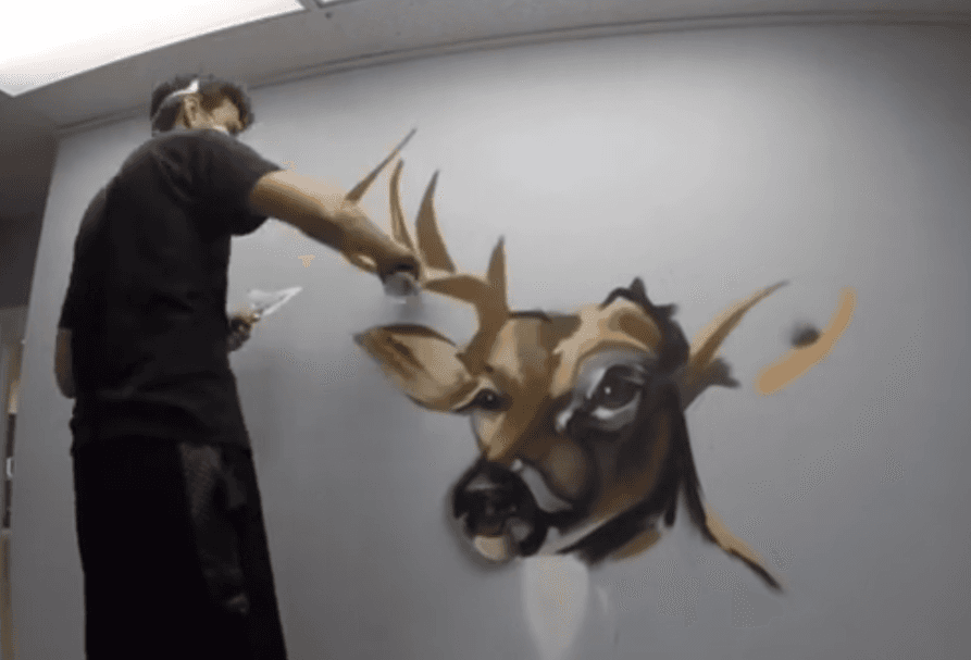 Mural artist spray painting a deer mural on an interior wall during the mural creation process