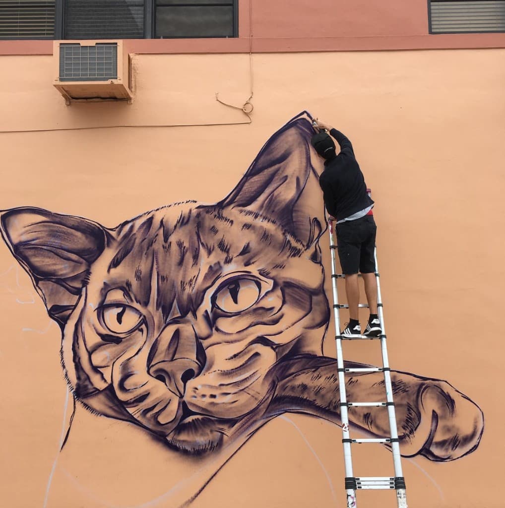 artist Mark Francis Bulk Styles outlining large cat mural during Paws on the Ave public art project in Lake Worth Beach Florida