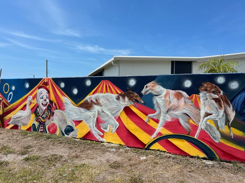 Wide view of circus themed mural featuring a clown, duck, and Borzoi dogs performing in front of circus tents painted by Mark Francis of Bulk Styles