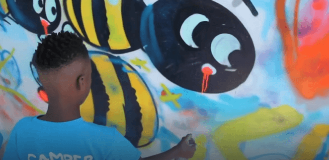 student spray painting a mural during the Lake Worth Beach Street Painting Festival youth art workshop led by mural artist Mark Francis