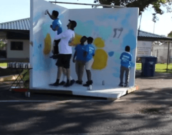 students painting a collaborative mural wall during the Lake Worth Beach Street Painting Festival youth art workshop led by mural artist Mark Francis