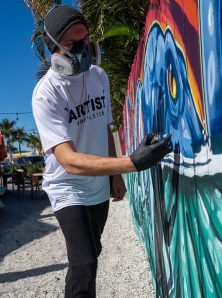 Mural artist Mark Francis (Bulk Styles) spray painting a colorful outdoor mural