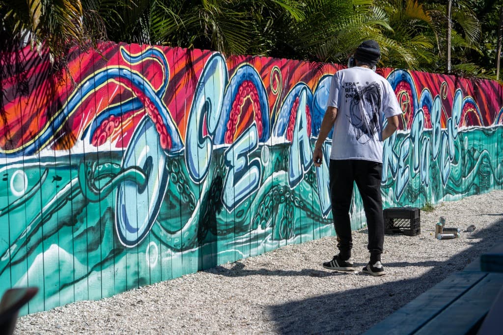 Mark Francis in front of a large, colorful ocean-themed mural on a wooden fence—community-scale public art